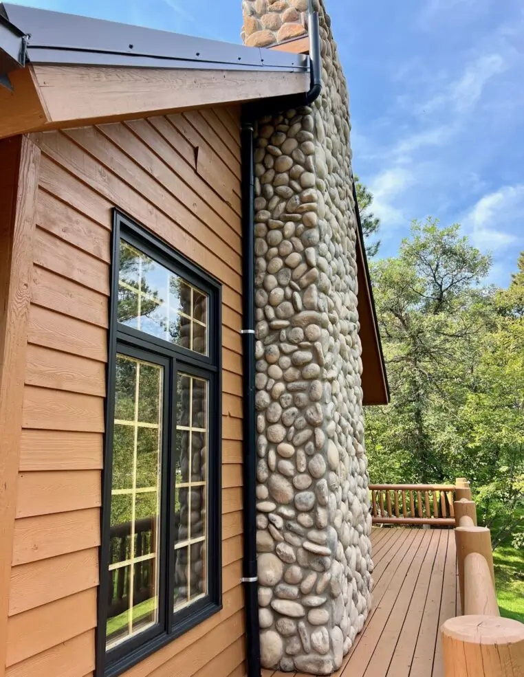 Black PVC radon mitigation system routed alongside the stone chimney of a custom home.