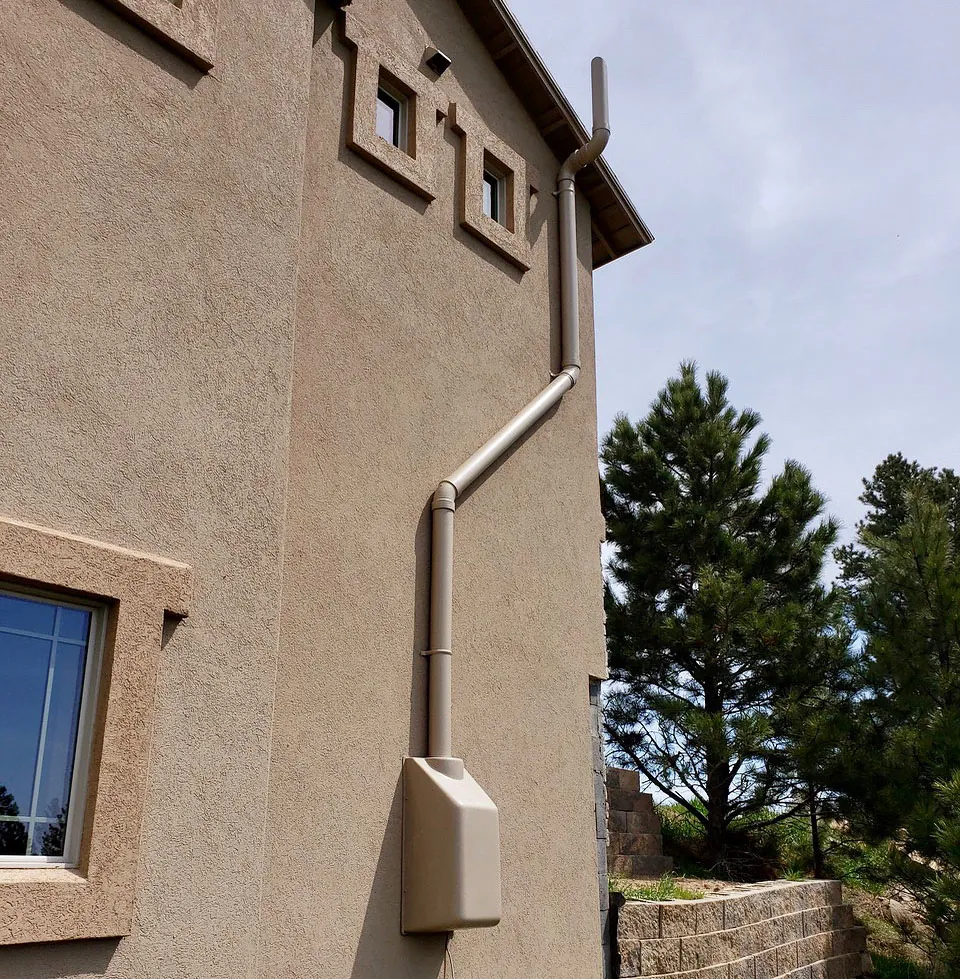 Custom radon mitigation system with color-matched exterior piping installed on a stucco home.