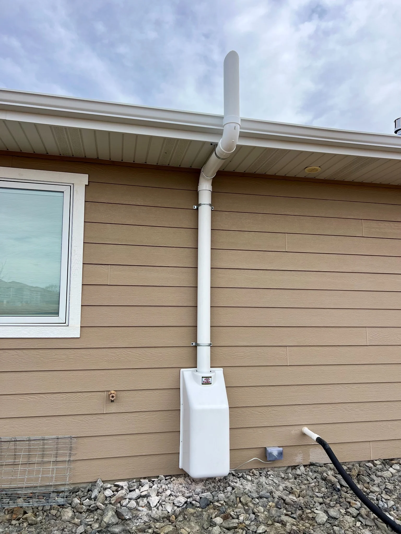 Exterior radon mitigation system with enclosed fan installed on a home in Rapid City, South Dakota.