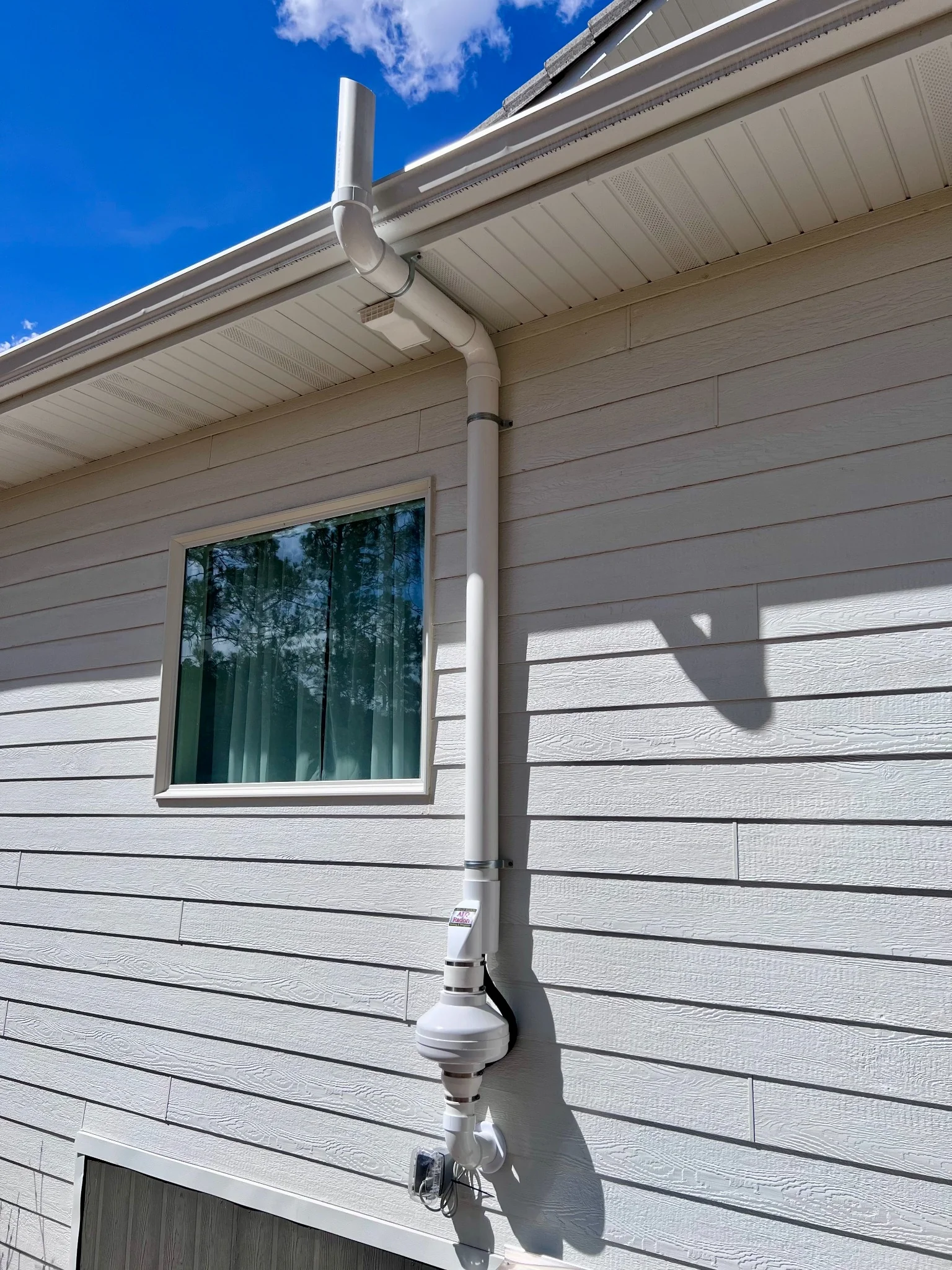 Exterior radon mitigation fan and vent piping installed on a home in Rapid City, South Dakota.