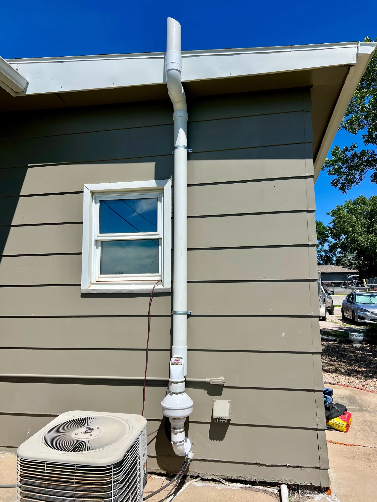 Residential radon mitigation system installed beside an existing air conditioning unit in Rapid City, South Dakota.